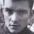Pixelated grayscale portrait of a person with dark hair and neutral expression, cropped to show upper face and shoulders.