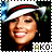 A pixelated image of a person wearing a white hat with red stripe, smiling with visible teeth, against a blurred background with green and blue tones.