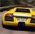 Yellow vehicle with dark windows and red taillights viewed from rear three-quarter angle on a blurred background.