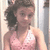 Pixelated image of a person with dark curly hair wearing a pink halter top, standing against light-colored vertical panels.
