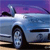 Pixelated image of a light blue car with a visible wheel, set against a purple and pink gradient sky background.