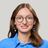 Pixelated static image of a person with long brown hair wearing glasses and a blue top against a light background.