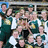 Group of people in green and white uniforms posing together with one person holding a trophy, pixelated image.