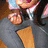 Pixelated close-up of a figure in dark clothing with light-colored hair, holding an orange object against a gray background.