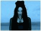 A woman with long dark hair and pale skin appears in two against a blue-toned background, her expression shifting from neutral to open-mouthed as wind blows her hair