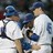 Two figures in white and blue uniforms embrace closely, one with a blue cap, against a dark background.
