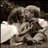 Pixelated grayscale image of two figures in close physical contact, one figure's head resting on the other's shoulder against a dark background.