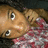 Pixelated close-up of a character with light brown skin, large eyes, and dark hair wearing a red patterned garment against a dark background.