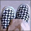 A pair of black-and-white checkered slip-on shoes with visible laces and a light-colored fabric background.