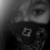 Black-and-white image of a person wearing a dark mask with a patterned bandana, showing eyes and forehead in a close-up view.