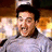 Pixelated image of a person with dark hair wearing a light-colored shirt, set against a warm-toned background with blurred light sources.
