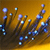 Pixelated abstract composition of blue and white dots on brown stems against a golden-brown gradient background.