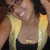 A person with dark curly hair wears a black top and yellow shawl, smiling with teeth visible in a of four