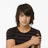 Pixelated static image of a person with short dark hair wearing a black striped shirt against a white background.