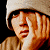 A pixelated contact sheet of two frames showing a person with light skin and dark hair wearing a beige beanie, one frame with hand near face and the other with hand covering mouth, next to green background with "Original Icons .com" text in bright green pixel font.