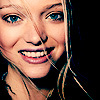 A close-up of a person with light brown hair, blue eyes, and a broad smile showing teeth, wearing a dark top with thin straps.