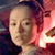 Pixelated close-up of a person with light skin tone, dark hair, and a neutral expression against a blurred background with red and dark tones.