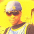 Pixelated image of a person wearing a white and purple cap, dark sunglasses, and a light-colored shirt against a bright yellow background.