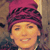 Static pixelated image of a person wearing a magenta headwrap with dark patterns, visible facial features including eyes and mouth, against a brownish background.