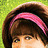 A pixelated close-up of a person's face with brown hair, a pink headband, and a green background.
