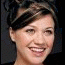 A static image of a person with short dark hair styled up, smiling against a black background with cursive text reading "Kelly Clarkson" in light brown.