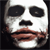 Pixelated face with large black eye sockets, white facial structure, and brownish-red mouth area against dark background.