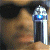 A 50x50 pixel animated buddy icon featuring a close-up of a person holding a silver and blue futuristic weapon against a dark background, with green text reading "Original Icons .com" on the right side.