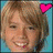A pixelated portrait of a smiling person with light brown hair, featuring two heart symbols on the head against a blue background.
