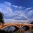 Pixelated landscape with bridge under cloudy sky on green background, pink text reads 'cry me a river, build me a bridge, and get over it!'