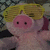 Pixelated pink pig with black eyes and a yellowish-brown hat, set against a dark background with indistinct shapes.