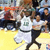 Two basketball players in mid-action on a court, one in white jersey with number 4 and black shorts, the other in green jersey and shorts. The player in white appears to be shooting or passing while the green-jerseyed player defends.