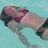 Pixelated image of a person lying on their back with arms raised, wearing a dark top and light shorts against a light blue background.