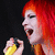 Pixelated image of a person with bright red hair holding a yellow object against dark background.