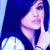 Pixelated image of a person with light skin and dark hair holding a microphone against a blue background with a white circular shape.