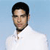 Pixelated image of a person with short dark hair wearing a white collared shirt against a light blue background.