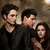 Three people in dark clothing stand together in a dimly lit setting with text reading NEW MOON! and 11.20.09 on a dark background.