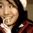 Pixelated close-up of a person with light skin, dark hair, and brown eyes wearing a white shirt under a red jacket, holding an object near their mouth.