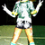 Animated figure in green and white patterned shirt, dark shorts, light blue shoes on grassy field with arms raised.