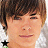 A pixelated close-up of a person with brown hair and light skin, wearing a white shirt with green accents.