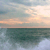 Pixelated static image of a sunset over water with gradient sky transitioning from light blue to orange and dark green sea below.