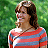 A pixelated image of a person with shoulder-length brown hair wearing a red and blue striped shirt against a green background.