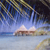 Pixelated static image shows a beach scene with palm trees, a small building, and water under a light blue sky.