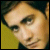 Pixelated close-up of a person's face with light skin tone, dark hair, and visible eyes against a yellow-green background.