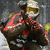 Pixelated figure in dark clothing with red accents holding a golden trophy against a gray background.