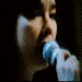showing a person singing into a microphone with mouth open and eyes closed against dark background