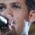 Pixelated close-up of a person's face with visible eyes, nose, mouth, and ear, wearing a white shirt and dark jacket, against a blurred background.