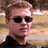 Pixelated static image of a person with light brown hair wearing dark sunglasses and a black top against a blurred background.