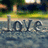 Pixelated image showing the word 'Love' in dark blue letters on a water-like surface with a blurred background of green and yellow tones.