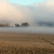 Pixelated landscape with brown terrain, light blue sky, and scattered dark gray structures under a hazy atmosphere.