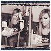 Two women seated at a table in a sepia-toned image, one resting her head on her hand while the other looks forward.
